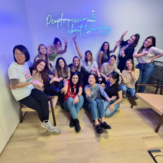Foto de grupo de participantes de Tech SHEssions posando en una sala de ERNI, con un neón en la pared trasera que dice "People passionate about technology".
