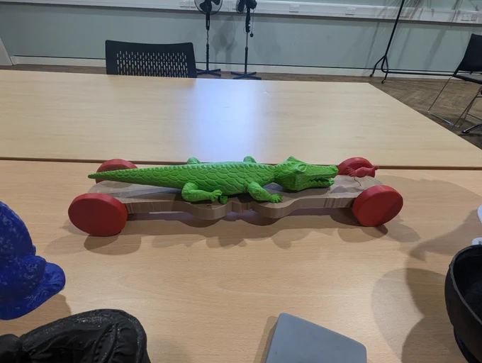 [A model of a crocodile looking at a model of a small chicken. Both are on a flat base with four wheels. The original object was made by a prisoner of war in WW1.]  