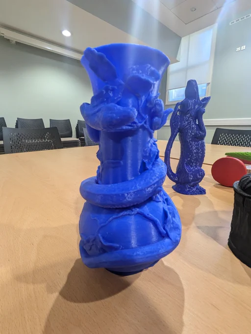[A blue 3D printed vase. The vase has a snake wrapped around it and intricate leaf designs all over it.] 