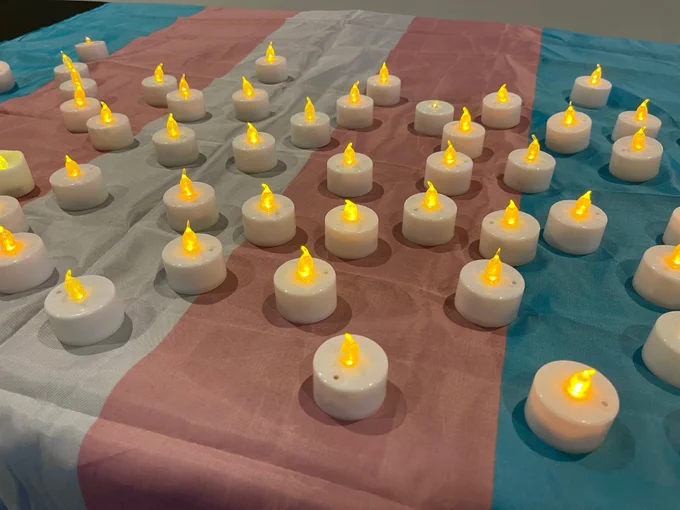A trans flag on a table with many electric tealight candles placed on top
