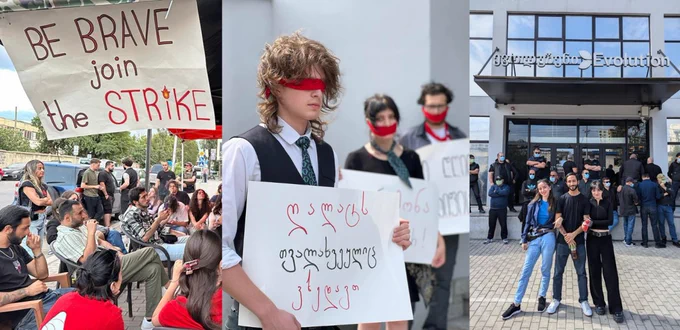 Striking workers wearing red blindfolds and mouthfolds. A large sign reads, "Be Brave Join The Strike." 