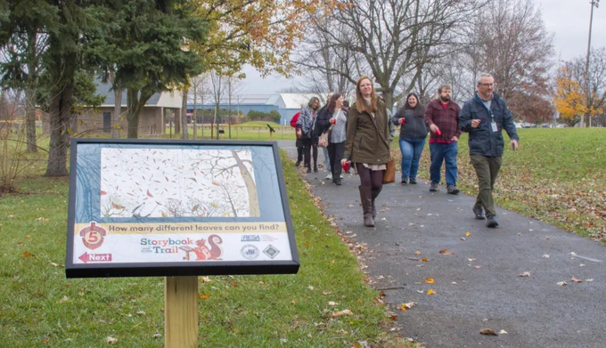 Ribbon cutting attendees walk along the Storybook Trail path towards one of the page displays.