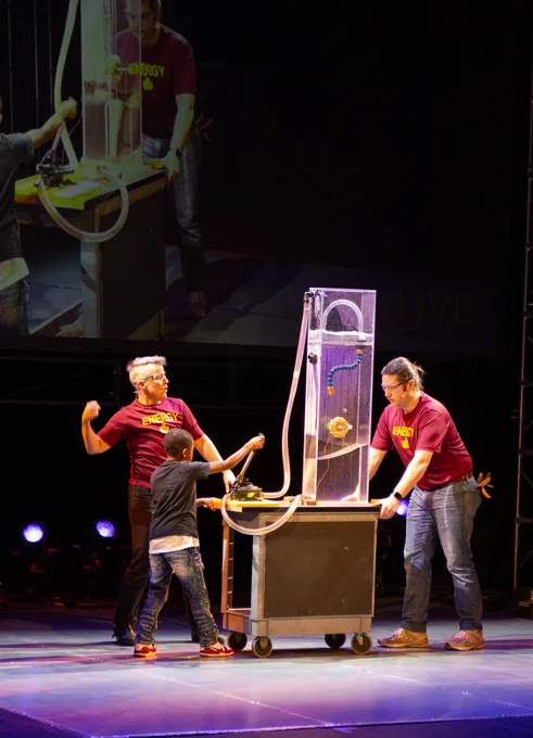 Two performers and a student conduct an experiment with water on a stage.