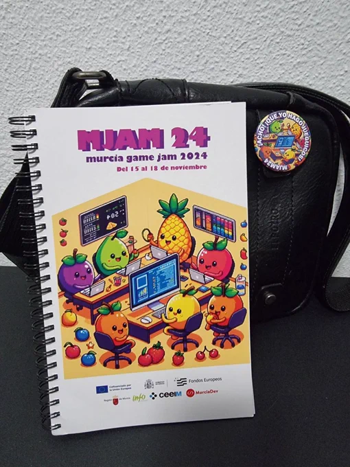 Bloc de notas y chapa de la Murcia game jam 2024.
En el dibujo hay frutas felices desarrollando con PCs.
Y en la chapa se exclama ¡Acho! ¡Qué yo hago jueguicos!