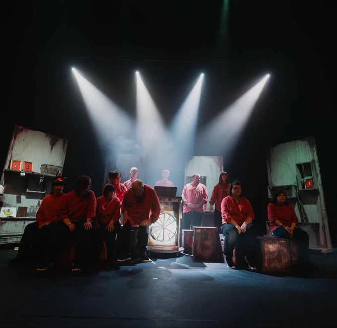 
The cast on the set of Storiescapes, some standing, some seated on boxes, in semi-darkness with four white spotlights focused in on them.
