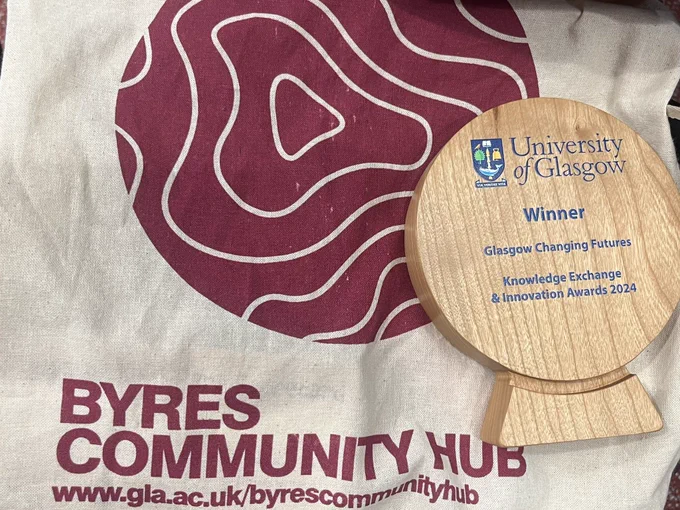 Round wooden trophy on a tote bag saying byres hub