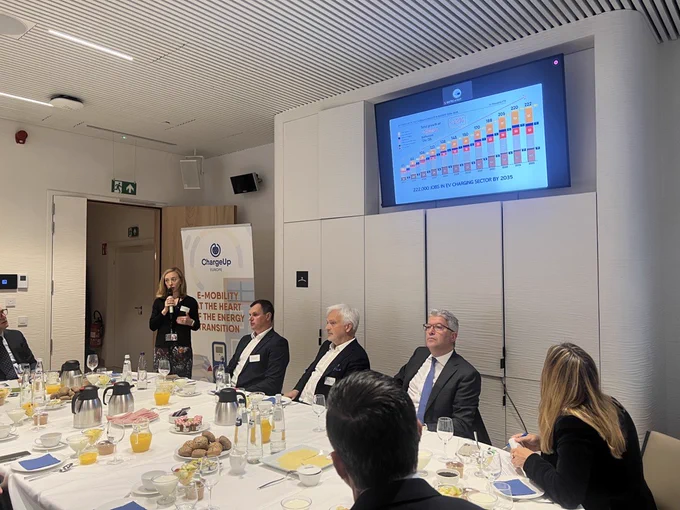 Lucie Mattera, secretary general of ChargeUp, stands in front of a projector screen displaying a graph showing predicted growth in number of jobs in the EV charging sector, which rises from 61,000 in 2024 to 222,000 in 2035.