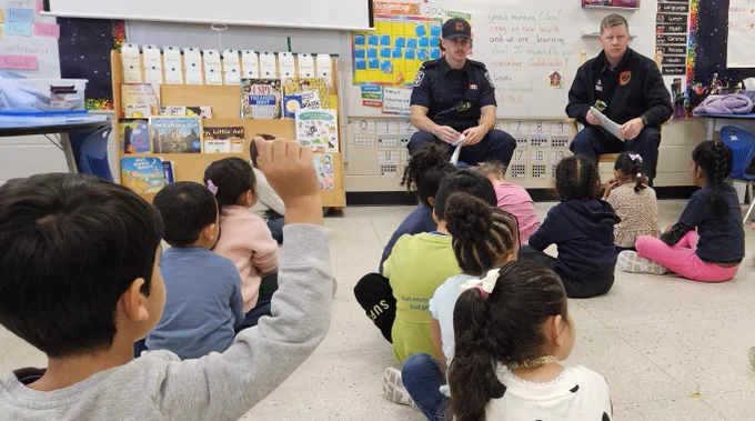 There are two firefighters sitting in front of students in a classroom.
