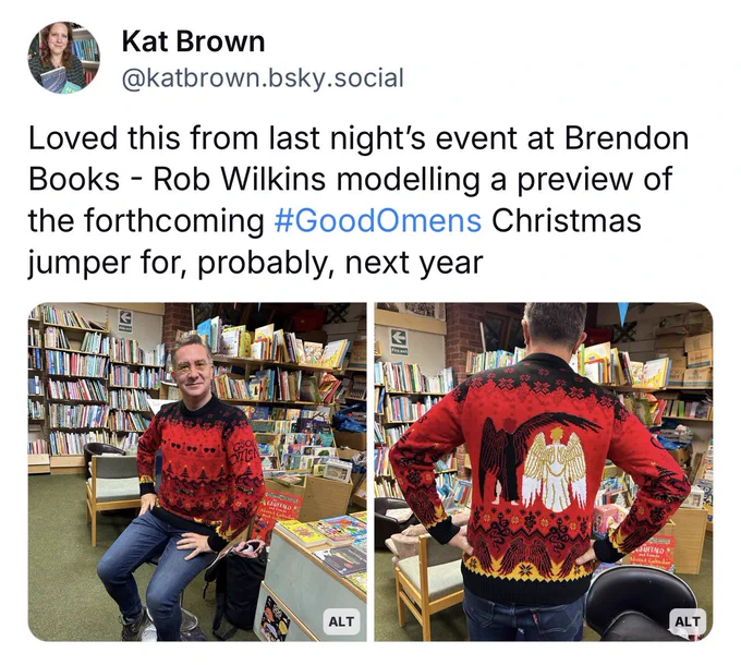 Kat Brown posted: “Loved this from last night's event at Brendon Books - Rob Wilkins modelling a preview of the forthcoming #GoodOmens Christmas jumper for, probably, next year”. Rob looking very holly jolly in a red, black and yellow jumper with repeat patterns of dark glasses and Christmas trees. On the back of the jumper are Crowley and Aziraphale and a repeat pattern of wings.