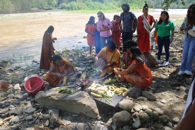 The IPON team after arriving at the San Pascual Ashaninka Indigenous community. The group are standing by the riverside around a small fire, with vegetables and meat on skewers, enjoying a traditional riverside barbecue. 