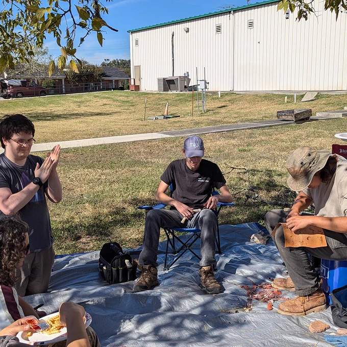 Some of the Archaeology Club members sitting outside of the Archaeology lab demonstrating and learning flint knapping.