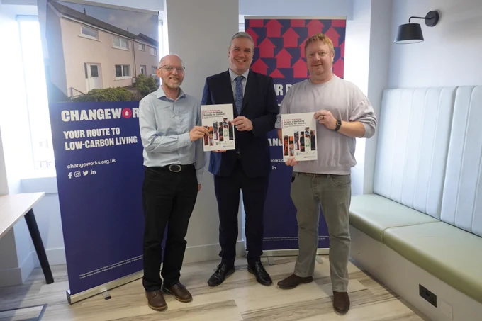 An image of the Investment Minister Tom Arthur standing in front of a Changeworks banner with two members of staff, holding copies of the Scottish Government's Social Enterprise Action Plan.