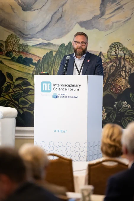 Phil Baty at a lectern giving a speech, with Interdisciplinary Science Forum branding
