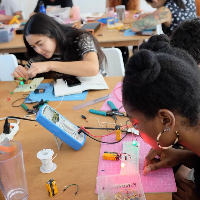 Two students work on circuits through breadboards and LEDS