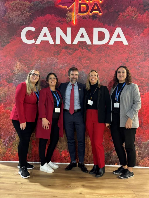Group photo featuring five individuals posing in front of a backdrop of red autumn foliage with the word "CANADA" prominently displayed. 