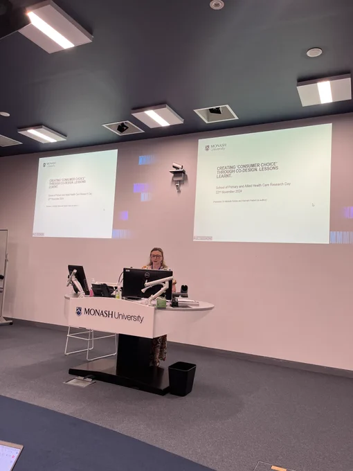 A person at a lectern with a dual screen behind them