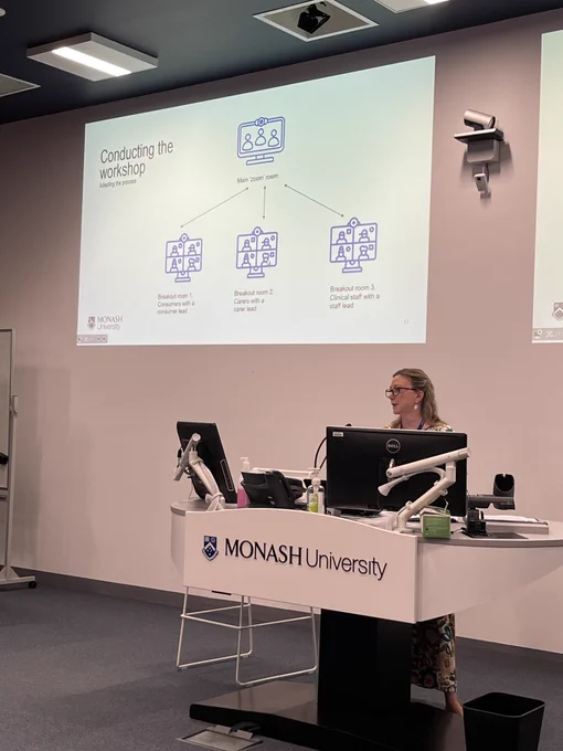 A person at a lectern with a dual screen behind them