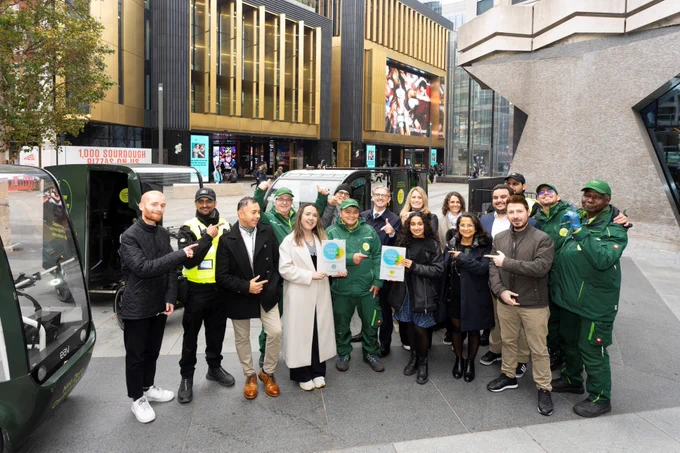 A photo of a team of people working for Central District Alliance, pictured outside their building with some of them holding Living Wage logos.