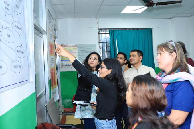 Member of a delegation of a high level mission standing and hearing the briefing of a woman pointing towards a paper chart.  