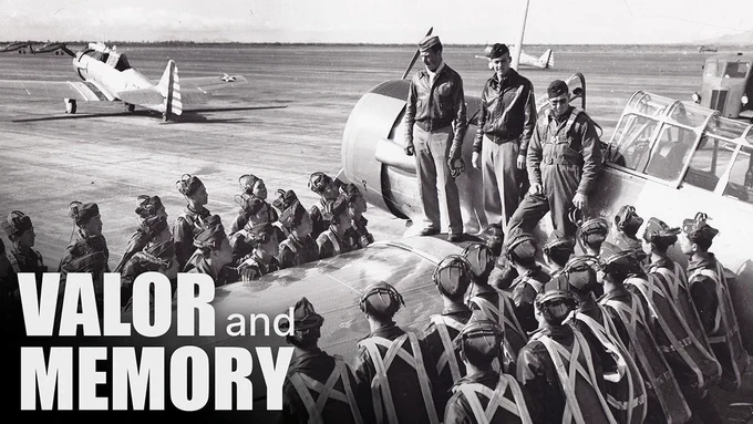 Photo from the documentary, "Valor & Memory," the story of the Flying Tigers, a heroic group of American military pilots who fought in China during WWII. A group of pilots in military gear circle around the wing of a fighter plane as thee men stand on top of the wing and address the group.