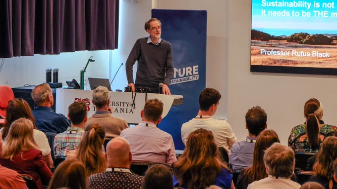 Professor Rufus Black Presenting at the ACTS Conference. He is standing at a lectern in front of a room of people. 