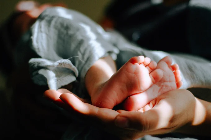 A baby being held, showing their feet in an adult's hands