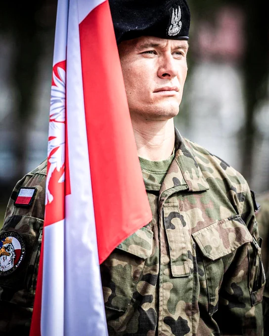 A Polish soldier holding the Polish flag. Photo by: NATO Multinational Brigade Latvia