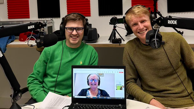 Paul and Tim in a podcast studio, with Jan shown on the screen of an open laptop joining them in a video call.