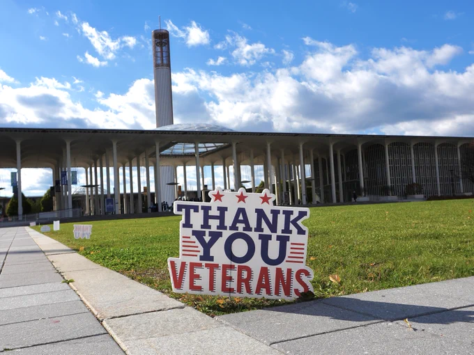 Sign reading "THANK YOU VETERANS" displayed on a lawn in front of UAlbany on a sunny day with clouds in the sky.