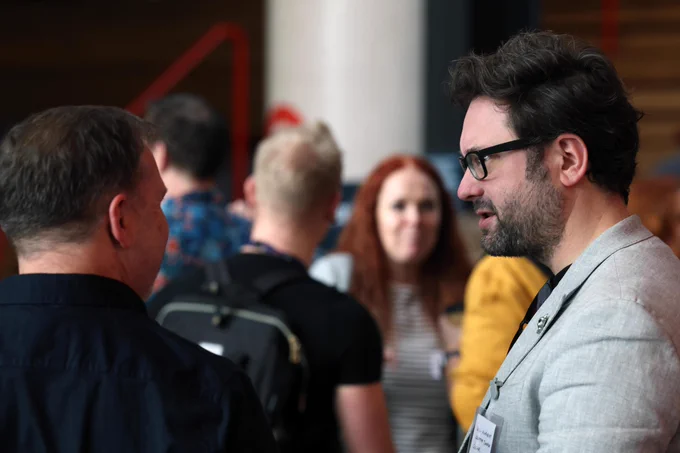 One person talking to another. There are other people blurred out in the background. 