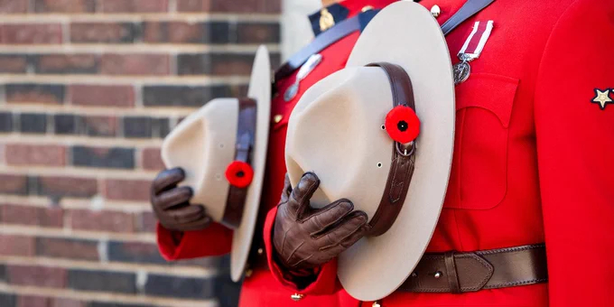 Two mounties in red serge hold Stetson hats with poppies against their chests. 