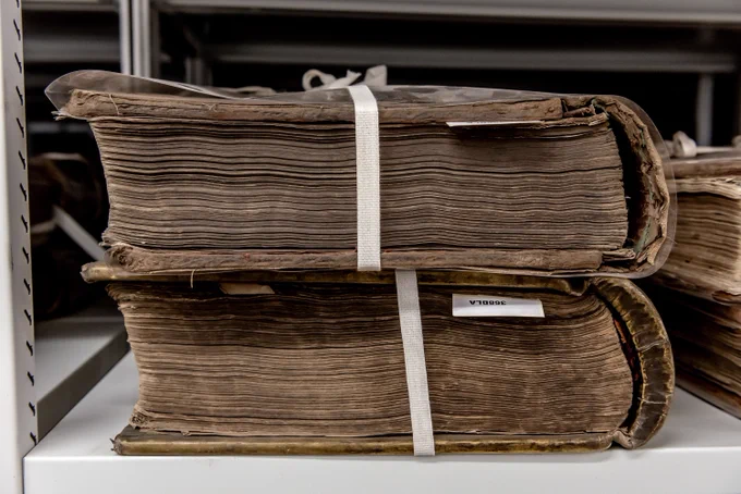 Two very large brown record books stacked on top of each other and  wrapped in white binding.