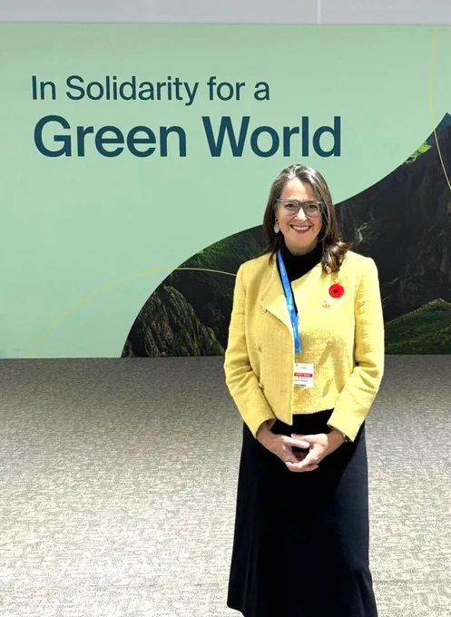 Canada’s Ambassador for Climate Change, Catherine Stewart standing in front of a mint backdrop written “In Solidarity for a Green World”. 
