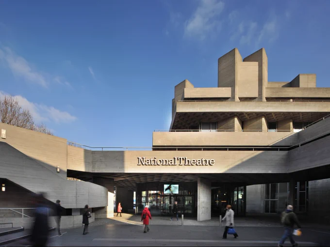 Exterior view of the National Theatre in London with people walking by in the foreground.