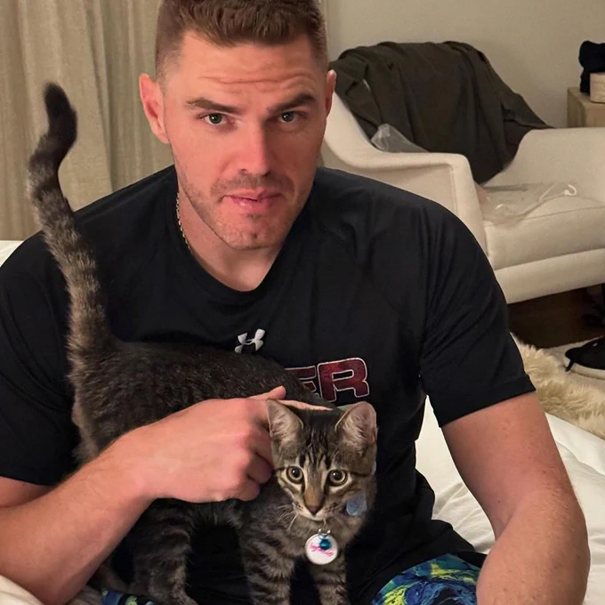 Freddie Freeman with a cat. He's wearing a black shirt with red letters on it. The cat has black and gray fur.