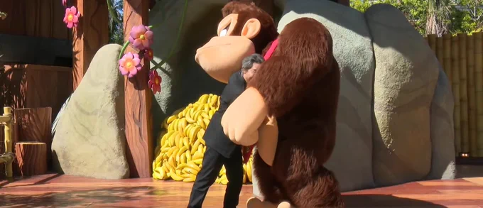 Shigeru Miyamoto hugs Donkey Kong near his banana hoard in Donkey Kong Country at Super Nintendo World.