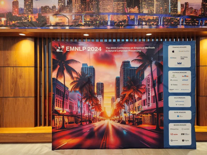 The EMNLP 2024 conference backdrop, showing the conference name at the top and a palm tree lined street at sunset, with sponsor logos on the right side.