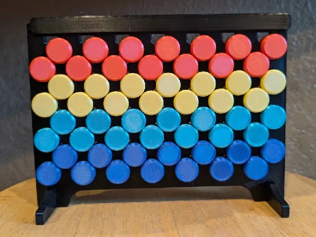 Photo of a 3D printed Zaggrivation board with red, yellow, light blue, and dark blue tokens on a black frame. The tokens are arranged to shift hue from red (top) to dark blue (bottom).