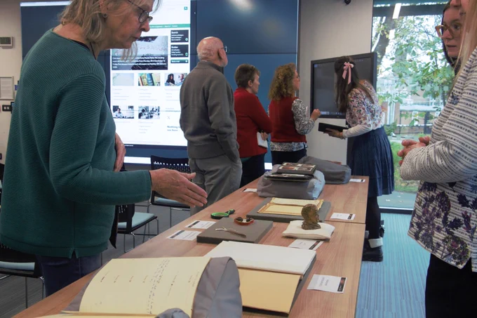 Visitors and archivists discussing archival items on display and looking a digital touchscreen in the background.