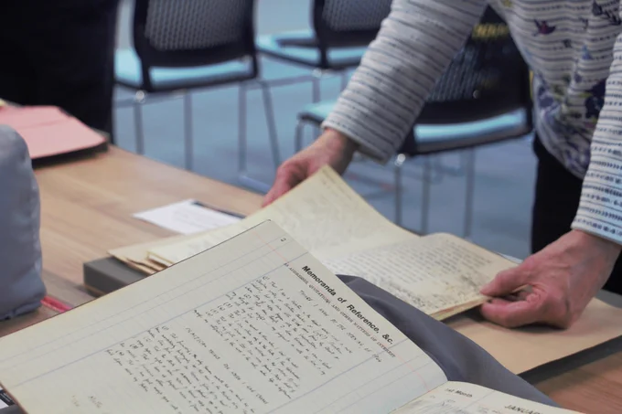 Zoomed in image of a person looking at a document from the Jack Clemo archive, with just their hands and arms showing. A diary of Jack Clemo is visible in the foreground.