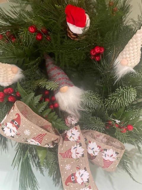 A festive flower arrangement, complete with Christmas ribbons, a bearded gnome and fake berries. 