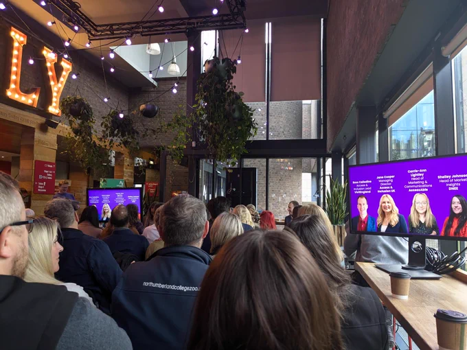 Group of people watching a presentation at Northern Stage for Purple Tuesday event. On the screen is the panel of speakers for the event.
