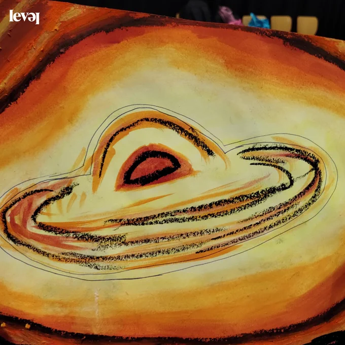 A close up of a pastel drawing. The drawing is of space and is in yellows, oranges and blacks. What looks like a planet with rings around it sits in the centre of the drawing.