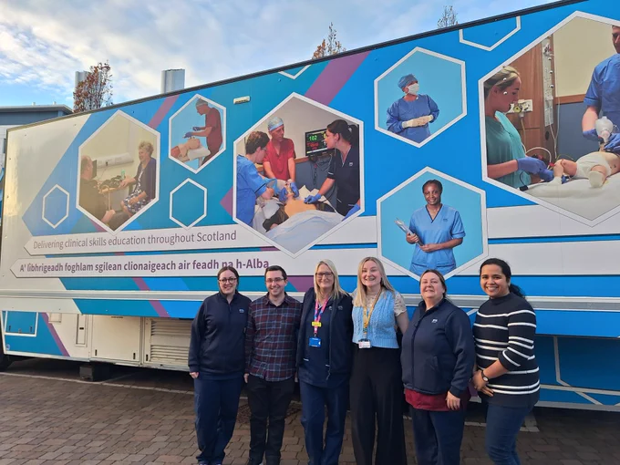 Six people standing in front of a clinical skills bus. Some are in medical uniform