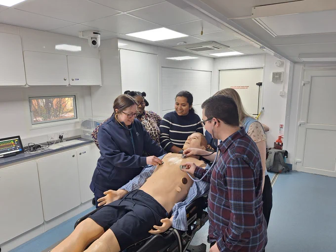 Six people surrounding a medical simulated patient in a skills lab