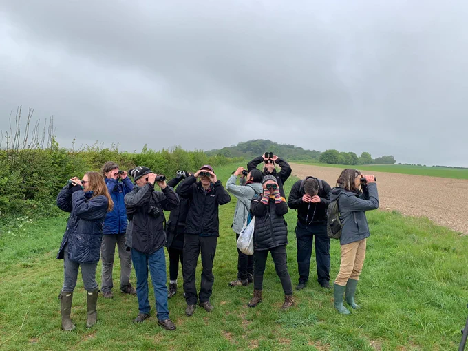 A group of people standing in a field using binoculars.
