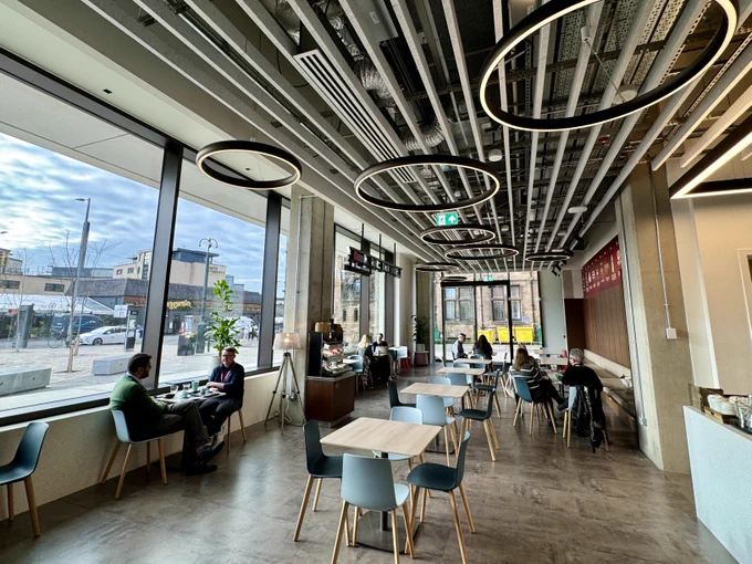 People sitting at tables in the new Tinderbox cafe in the Adam Smith Building. Dumbarton Road can be seen out the windows in the background. 