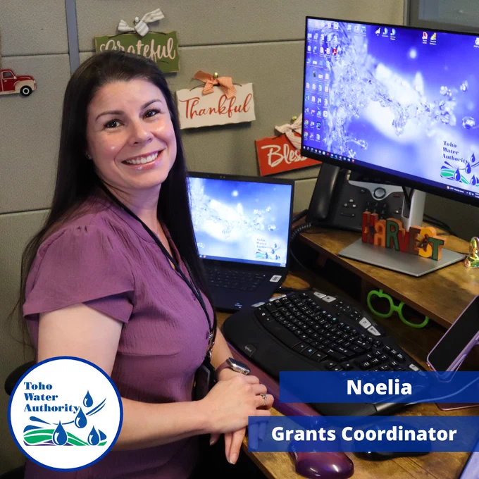 A photo of Noelia, Toho's Grants Coordinator, sitting next to her desk. The words "Noelia" and "Grants Coordinator" are located in the bottom right in blue rectangles. The Toho logo is located in the bottom left. 