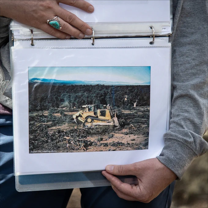 A person holds a photo a bulldozer after it finished tearing down pinyon pine forests. 