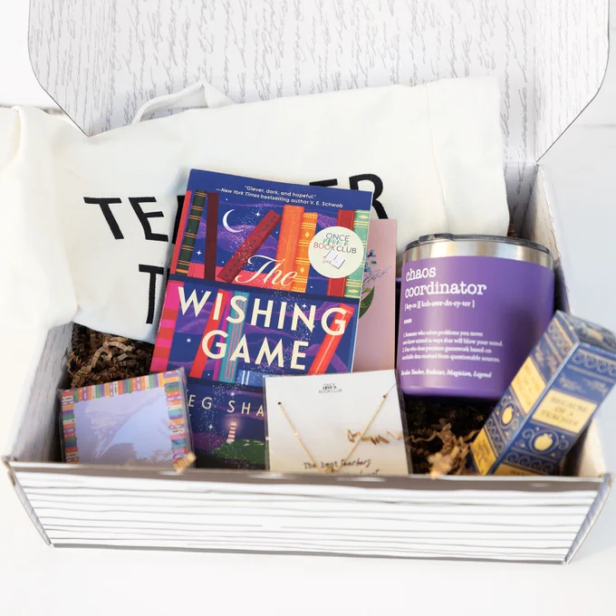 An open box with a book, mug, sticky notes, necklace, box, and tote bag